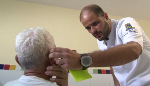 Médico tocando a orelha de um paciente idoso, que está de costas (Foto: Reprodução da UFC TV)