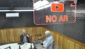 Estúdio de rádio, com duas pessoas ao microfone. O foco está na placa de "No Ar" (Foto: Guilherme Braga/UFC)