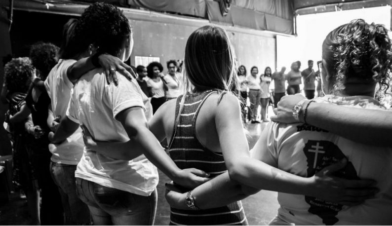 Grupo de mulheres abraçadas de costas, formando uma espécie de cordão humano (Foto: Rosilene Miliotti/FASE)