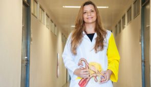 Professora Tatiana Zylberberg em um corredor segurando um peça anatômica que reproduz um útero (Foto: Viktor Braga/UFC)