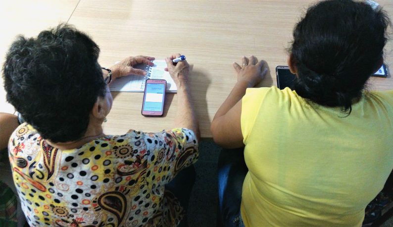Duas mulheres de costas, com um celular sobre a mesa