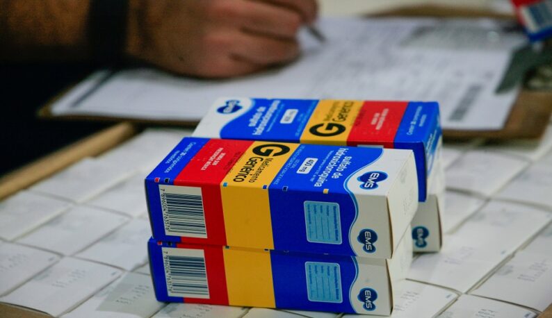 Em primeiro plano, caixas de sulfato de hidroxicloroquina sobre uma caixa; em segundo plano, há a mão de uma pessoa fazendo anotações em uma prancheta (Foto: Jader Paes/Agência Pará)