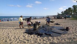 Fotografia de pessoas retirando óleo da areia da praia