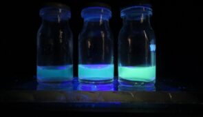 Três frascos com líquido azul fosforescente, com a cor ficando mais forte nos fracos da esquerda para a direita; o fundo é preto para destacar a cor