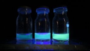 Três fracos com líquido azul fosforescente, com a cor ficando mais forte nos fracos da esquerda para a direita; o fundo é preto para destacar a cor