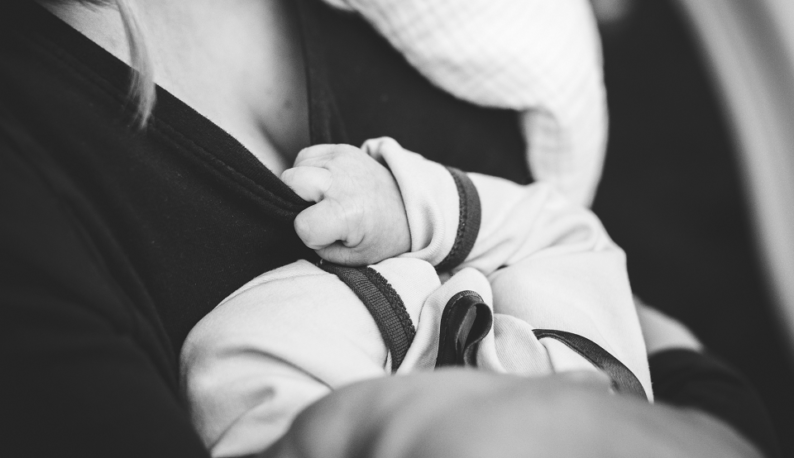 Foto em P&B de bebê agarrando o peito da mãe para mamar