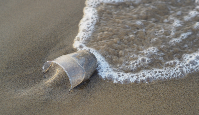 Copo de plástico descartável na areia da praia, com água do mar o molhando