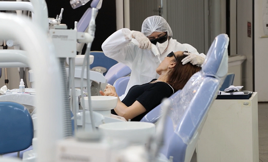 Paciente deitada em cadeira tendo laser aplicado na boca por enfermeira