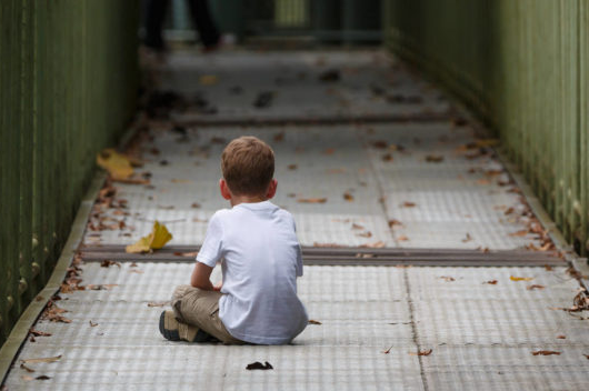 Imagem de criança sentada sozinha num corredor