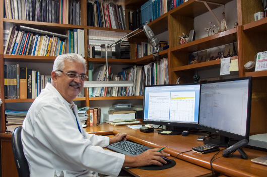 Imagem: Prof. Aldo Ângelo Moreira Lima sentado em escritório, frente a um computador