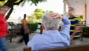 Homem idoso sentado com as mãos na cabeça