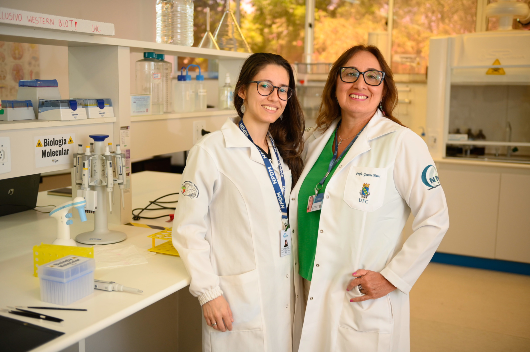 Pesquisadoras usando jaleco posam para foto em laboratório