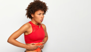 Mulher de blusa vermelha com expressão de dor, apertando a barriga