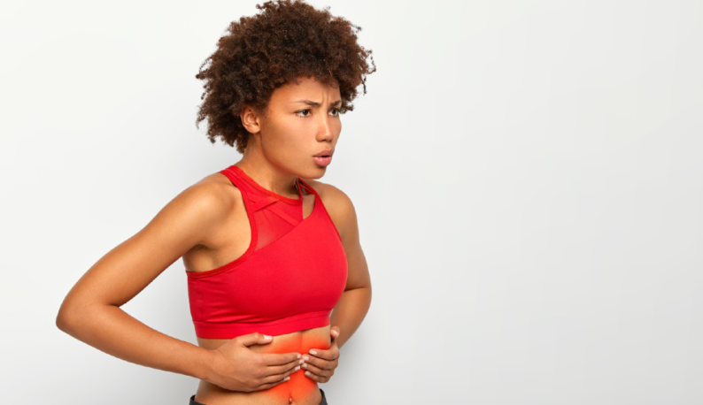 Mulher de blusa vermelha com expressão de dor, apertando a barriga