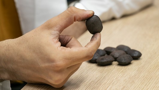 Imagem de uma mão segurando um briquete, com vários outros sobre uma mesa
