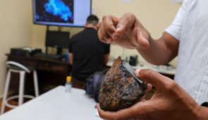 Foto de pesquisador em laboratório segurando uma rocha e apontando a presença de cobalto