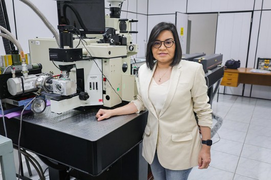 Fotografia da professora Lucilene Santos, do Departamento de Geologia da UFC, ao lado de equipamento de beneficiamento de grafite em laboratório da universidade (Foto: Ribamar Neto/UFC)