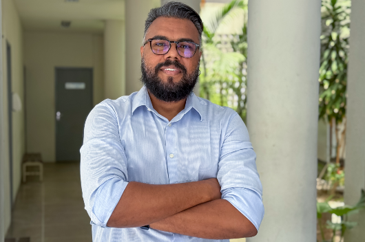 Imagem do professor Júlio Araújo de braços cruzados em um corredor da Universidade