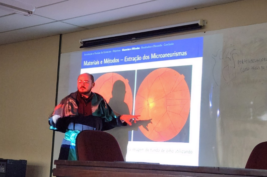 Pesquisador apresenta pesquisa em defesa de doutorado, usando veste talar